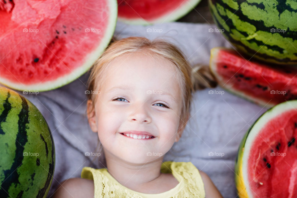 Portrait of happy little girl with blonde hair which lying near watermelons