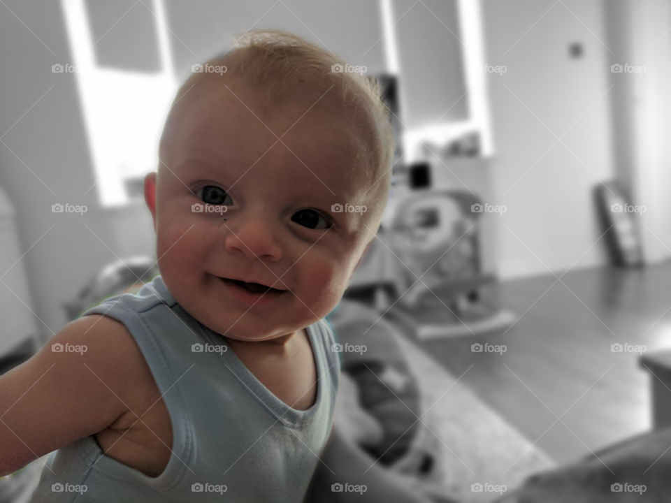 Baby Oliver smiles at the camera. Black and white background. 