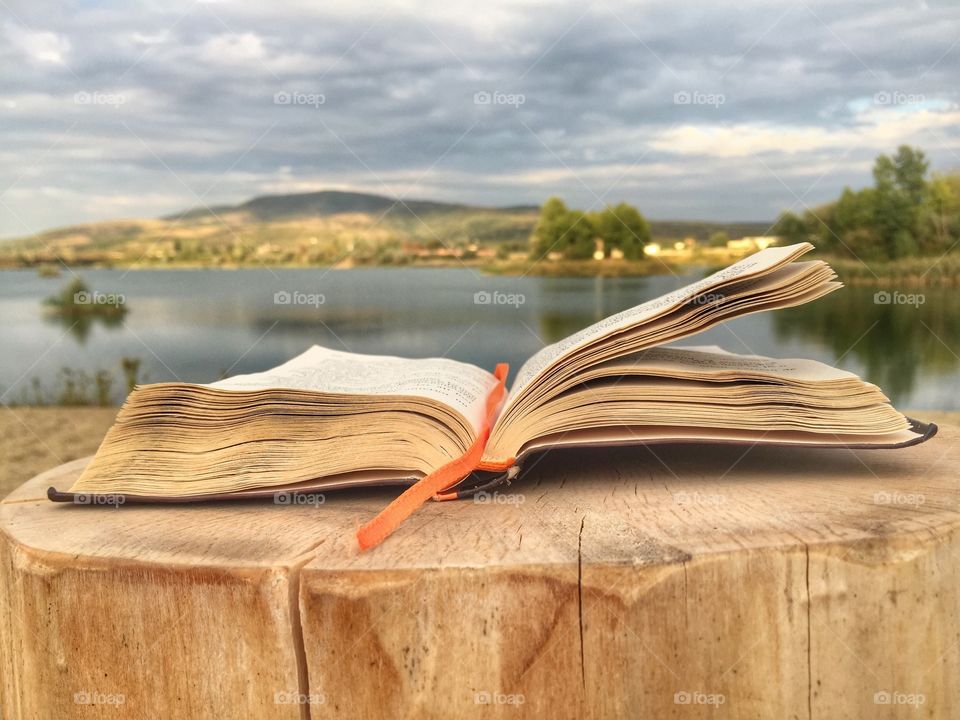 Open book sitting on wooden table with view of lake in front 
