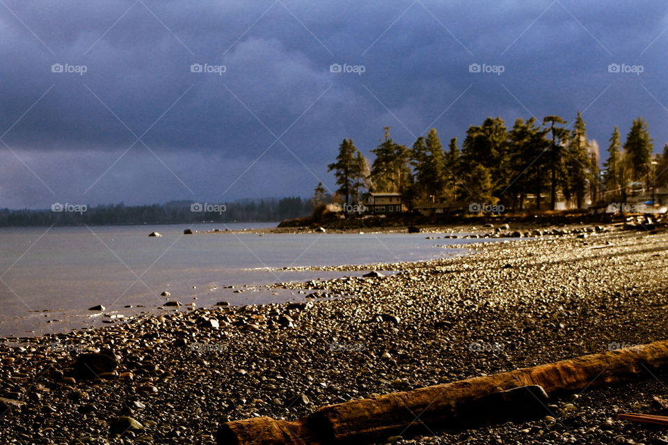 The sun poked a hole in the dark blue stormy sky to light up the shoreline with a golden glistening glow.