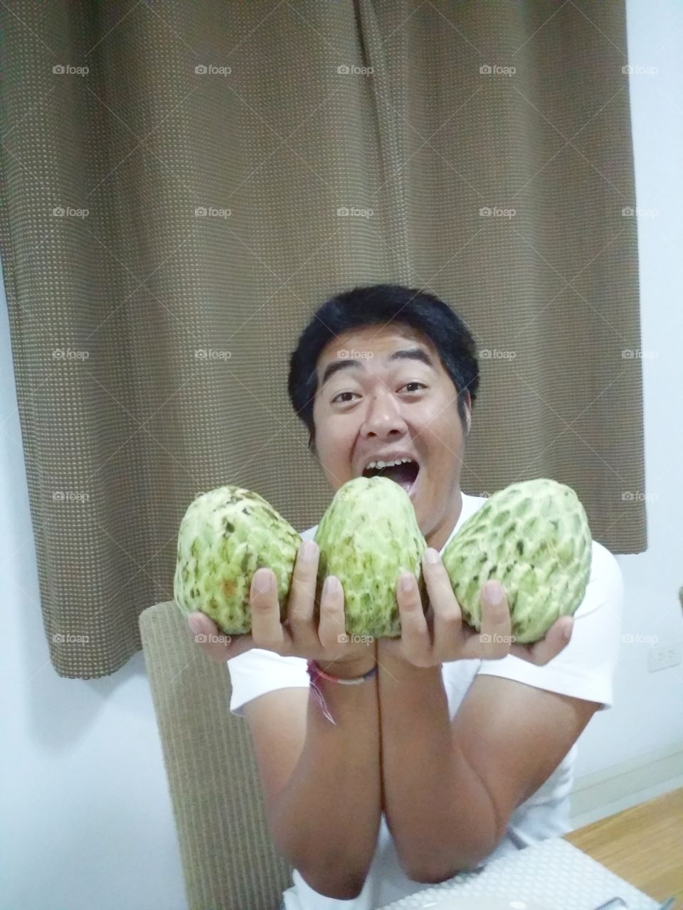 The man was happily showing 3 custard apple while resting in his house.