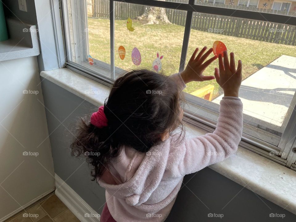 Toddler girl hangs up Easter stickers on window, decorating for Easter, little girl helps mommy, decorating the house for Easter 