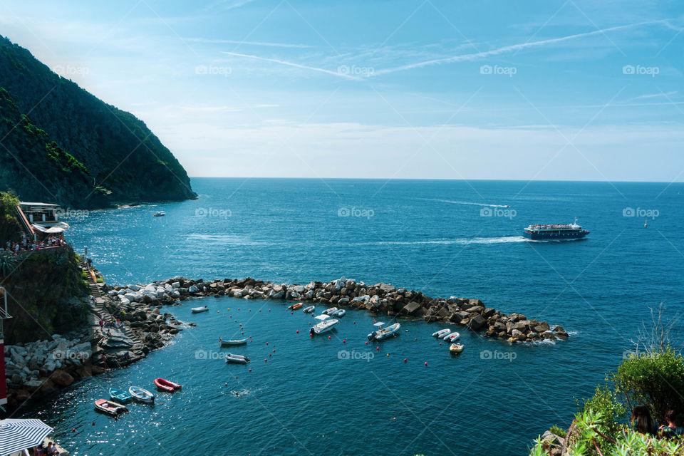 The sea view from the Cinque Terre. The boats sail between the waters and the rocks. A small house overlooking the sea colors the view.