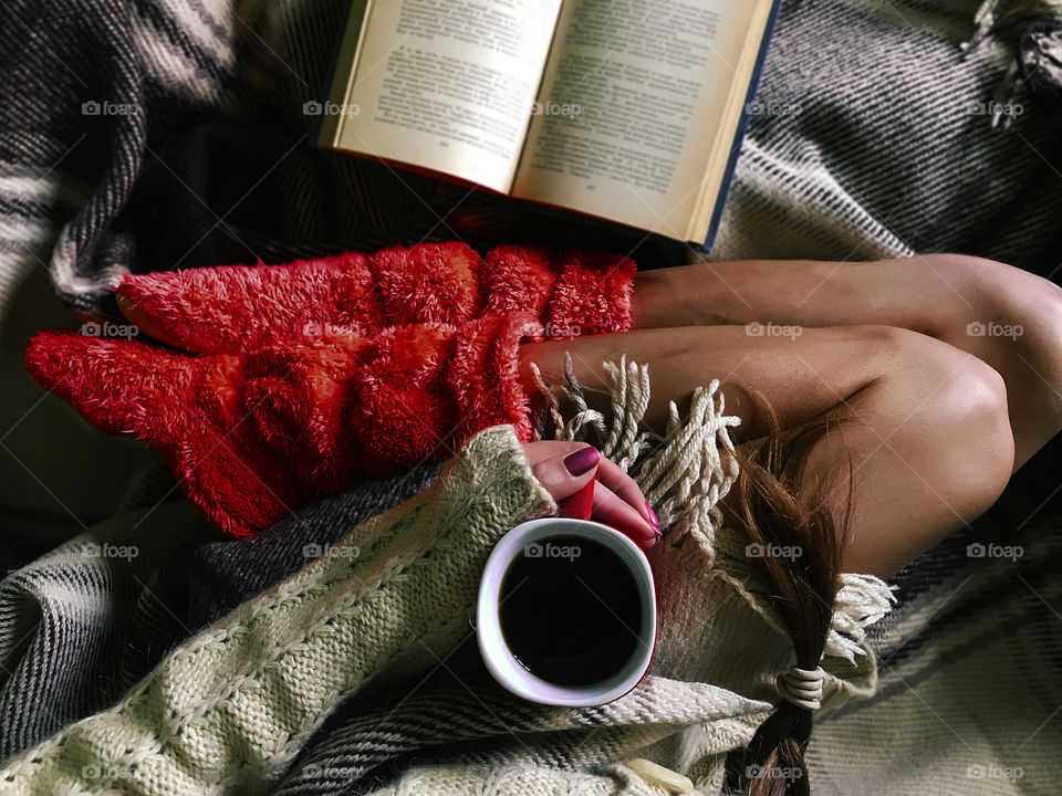 Overheard view of a young woman drinking coffee in cozy bed with a book 