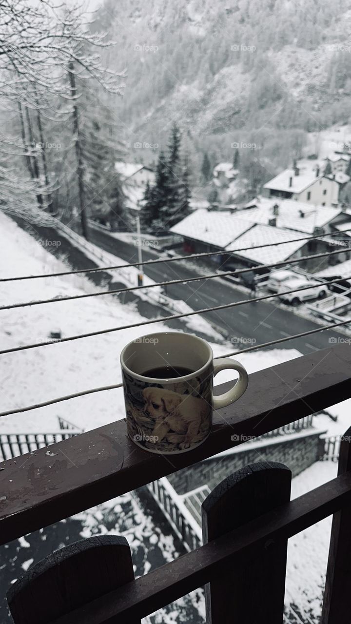 A cup of hot coffee on the wooden banister in winter landscape 