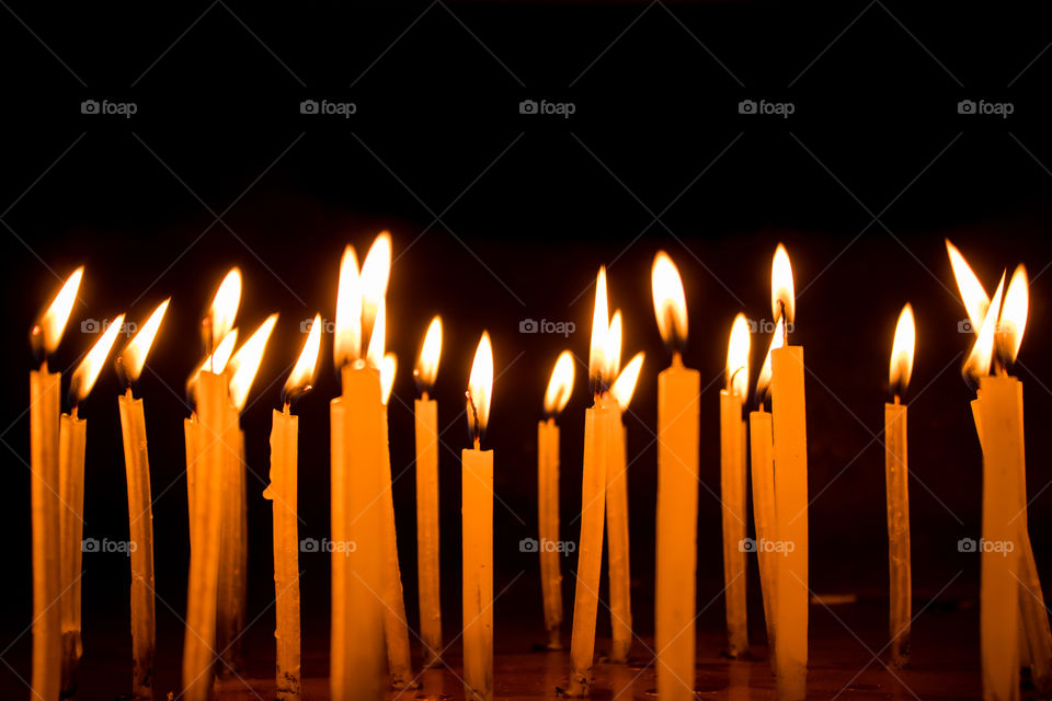 Many Christmas candles burning at night on the black background. Candle flame set isolated in black background. Group of burning candles in dark with shallow depth of field. Close-up. Free space.