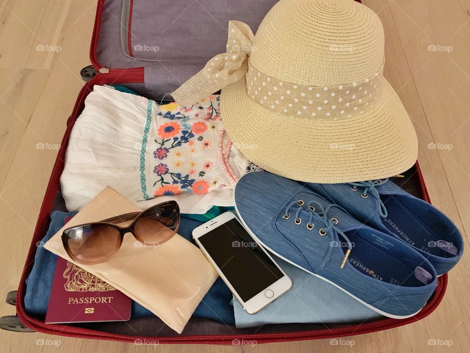 Suitcase with summer clothes, hat, passport, phone, shoes and cooling glass 