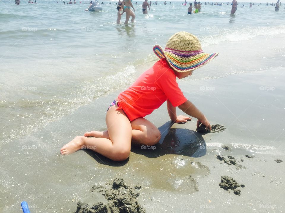 Little girl sitting at beach playing with wet sand