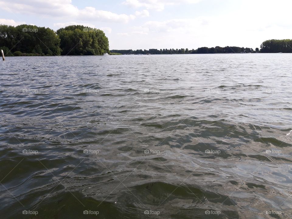 Uitzicht over het water, een Meer. Grote groene bomen op de achtergrond, ook wat bewolkt in de lucht. Nederland.