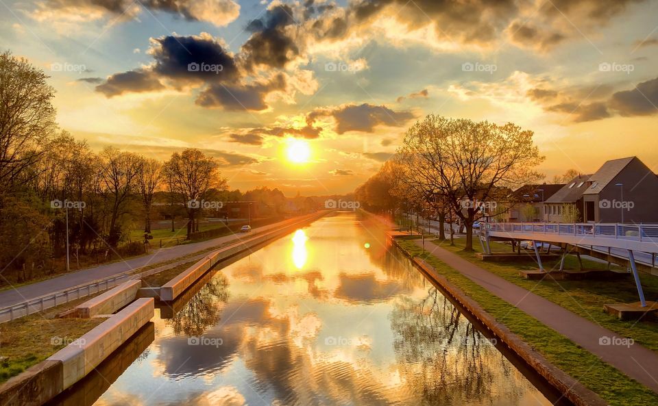 Golden sunrise or sunset with Fluffy white and dark clouds over a Countryside landscape reflected in the water of the river or canal