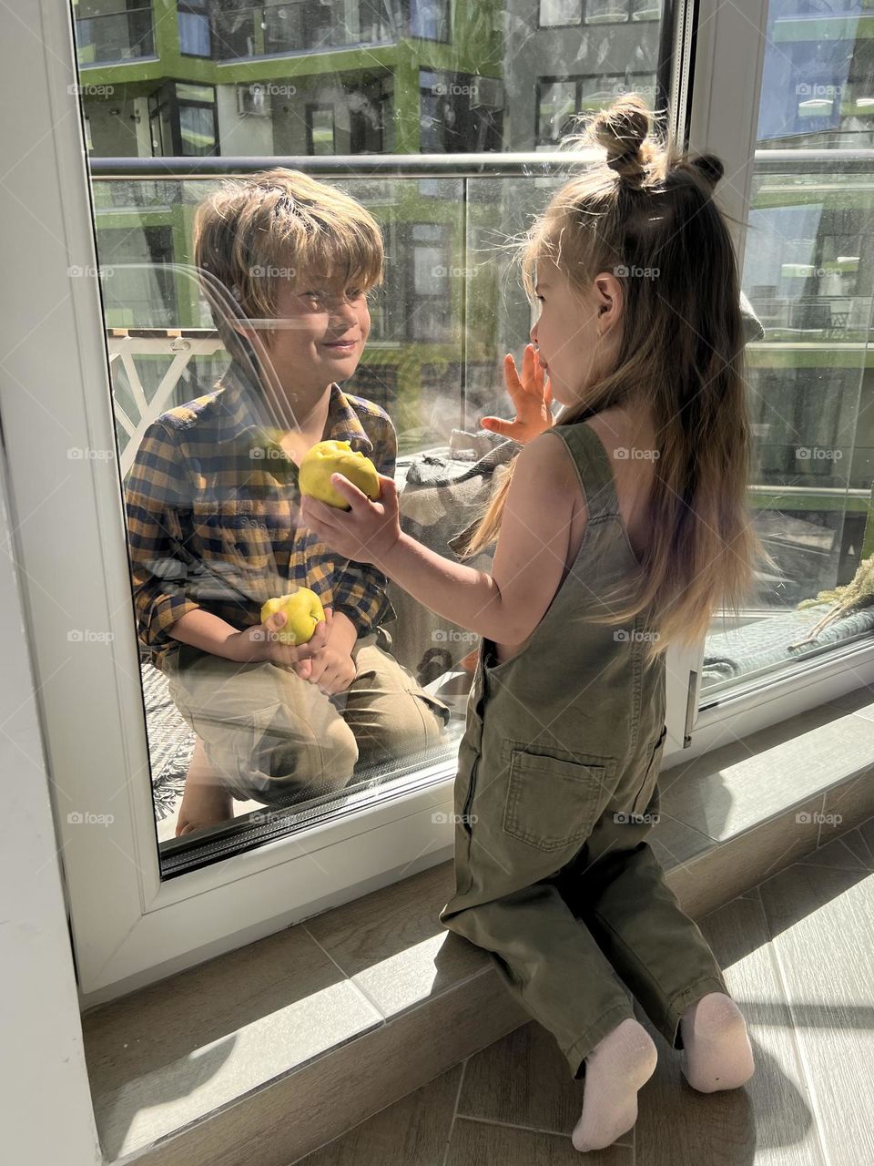 two children, on opposite sides of the window, look at each other