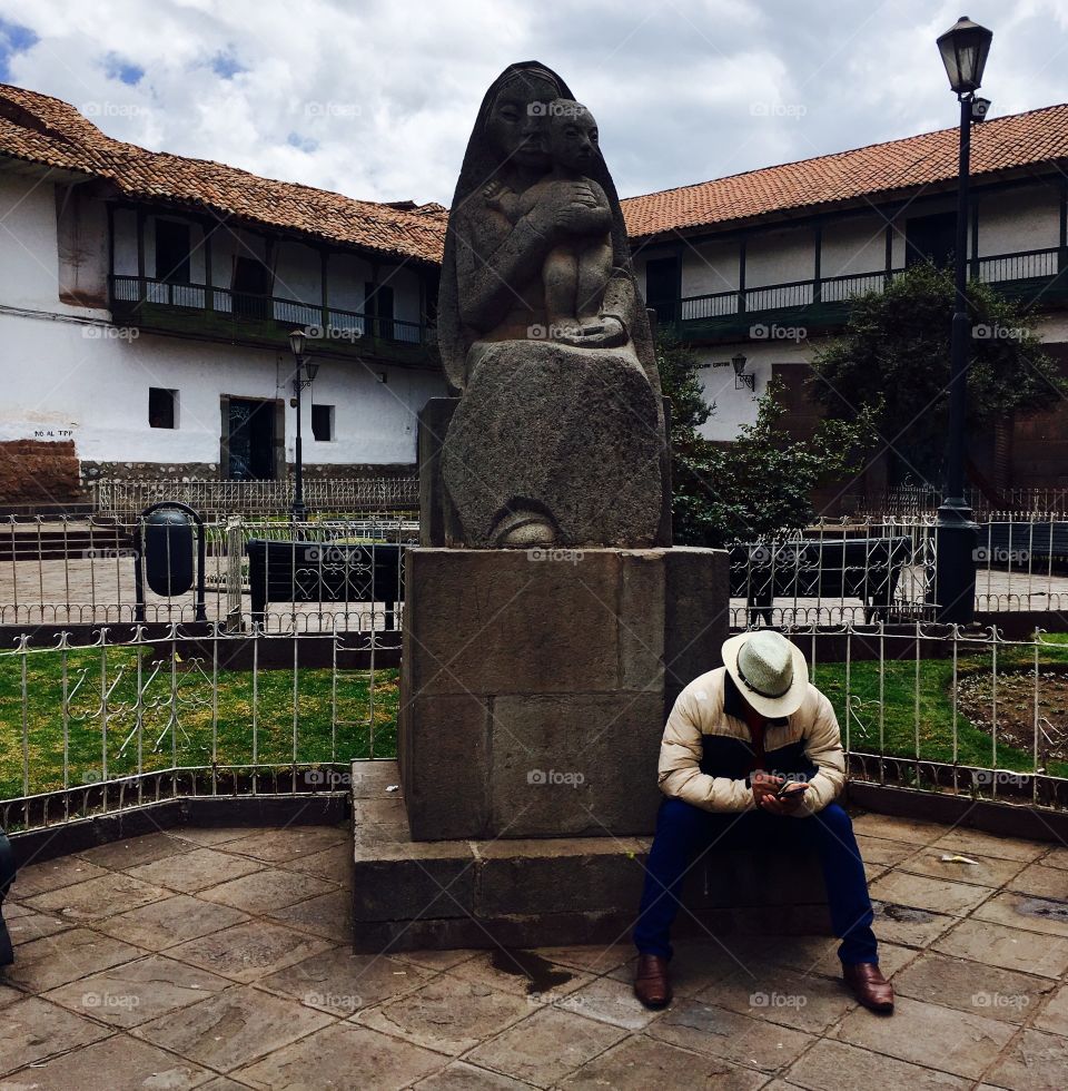 A Peruvian cowboy rests next to a statue in Cuzco