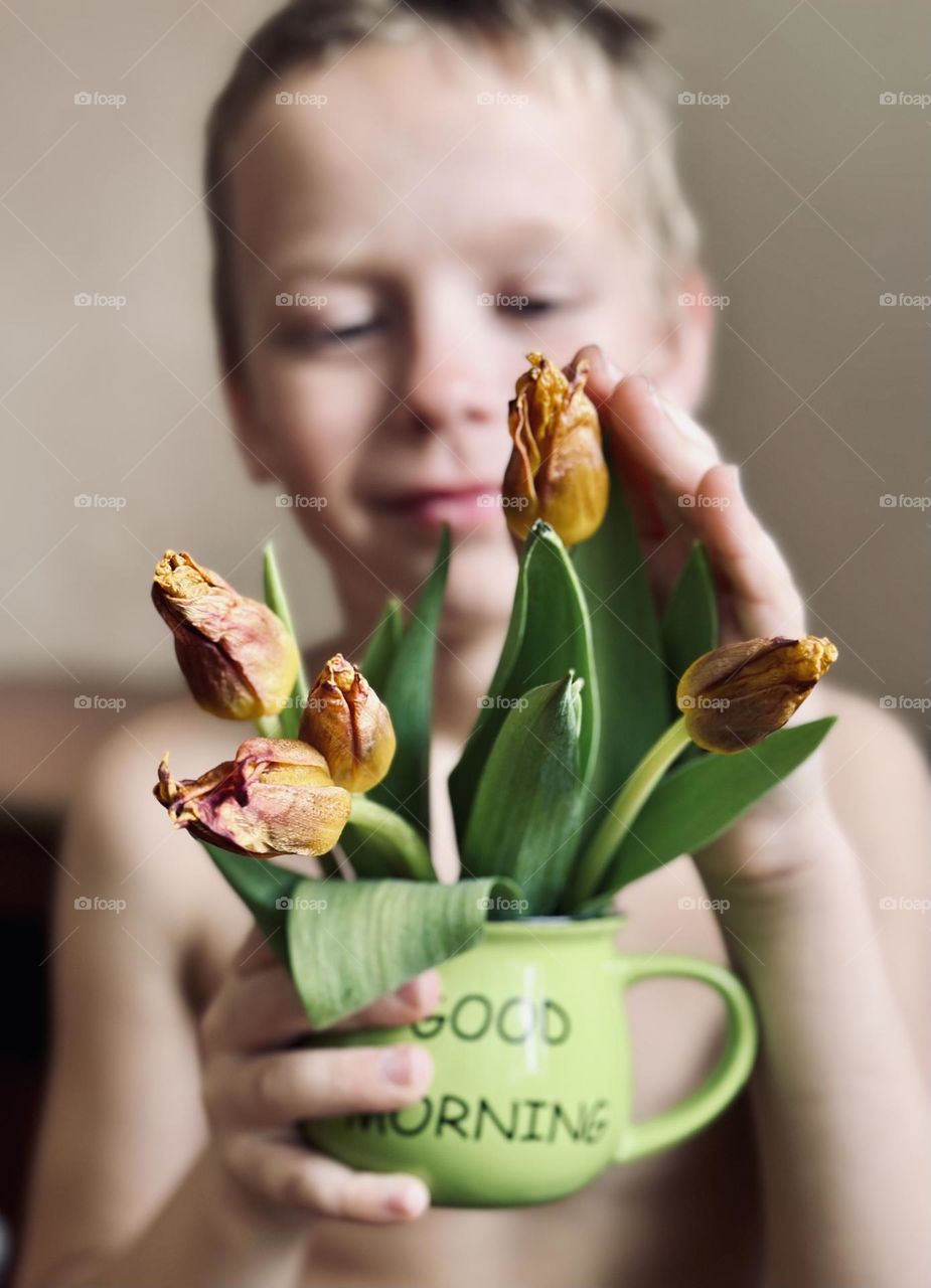 The boy is holding a mug of tulips