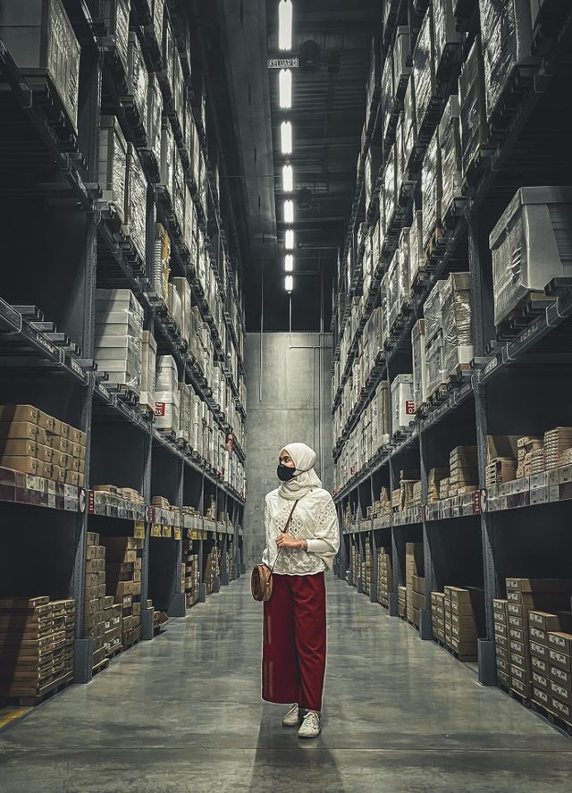 A girls standing in the middle of tall shelves and boxes in a warehouse 