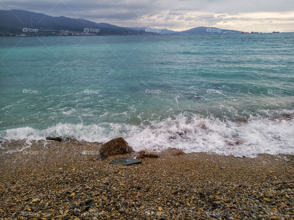 Sea, waves, and heavy rain. Pebble beach. Mountain range.