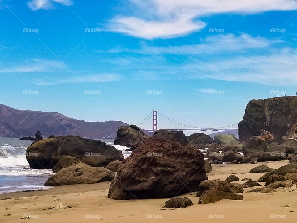 View of the Golden Gate Bridge from Lands End Beach through the rocks on a clear day with blue skies and just a wisp of clouds 