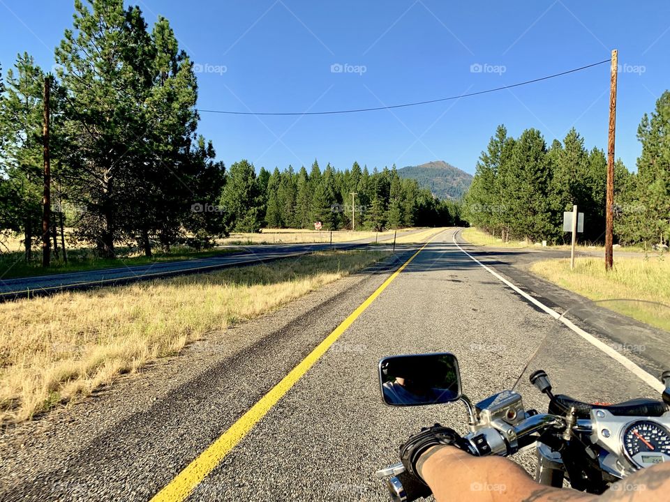 Riding a Honda VTX 1800 down a stretch of back road, seeing forest and grasses along both sides of the road and mountains in the background.