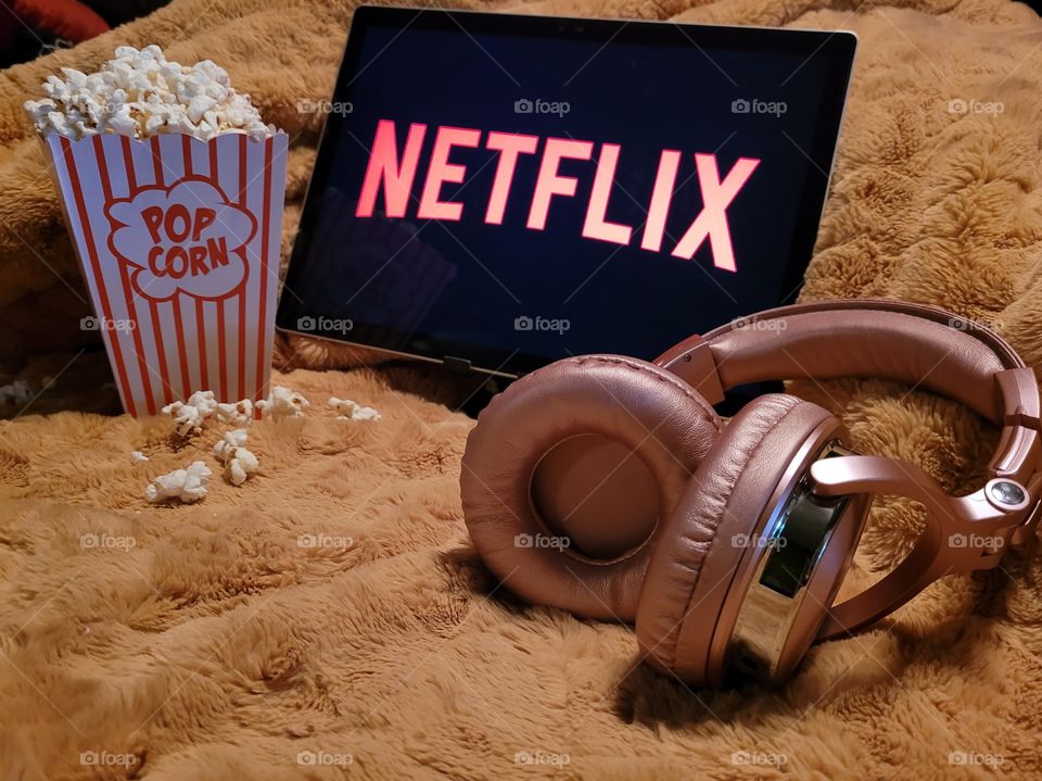 Laptop computer screen ready to watch Netflix for a fun, cozy, and relaxing night with popcorn as a snack, on soft bed blanket in room, with pink headphones