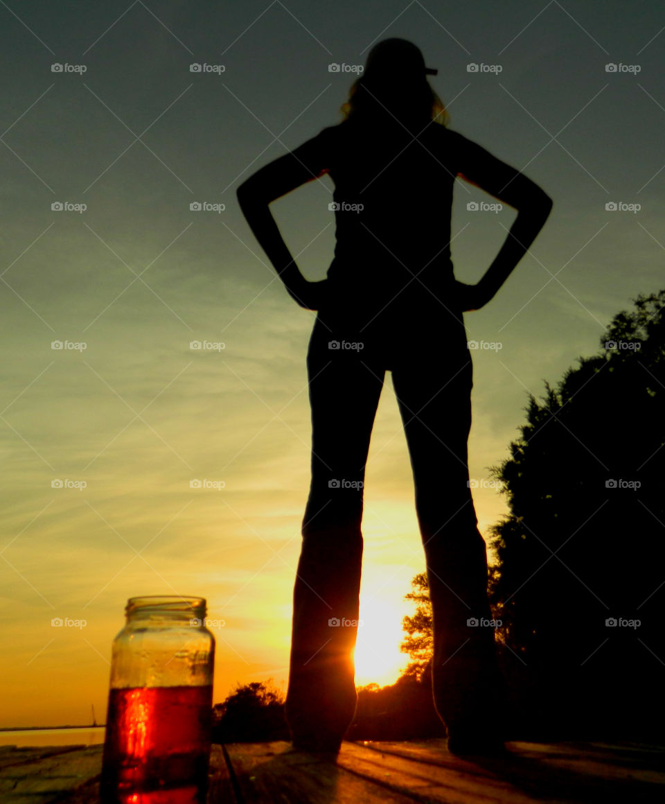 Slender Sunset. 
Sunset,women,standing,tall,hands on hips,looking at sunset,nature,trees,sun,landscape,silhouette 
