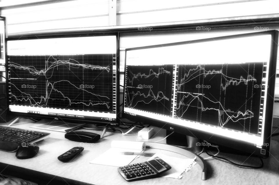 Rectangles of stock charts on computer screens a calculator remote eye glass case note pad keyboard and metal door