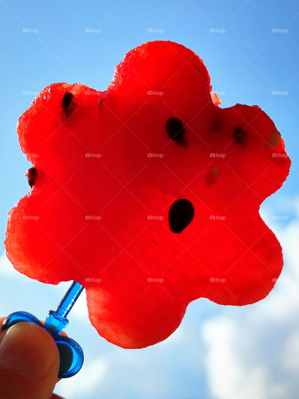 Red color.  hand holds on a blue spage a red flower cut from a watermelon against a background of clear blue sky