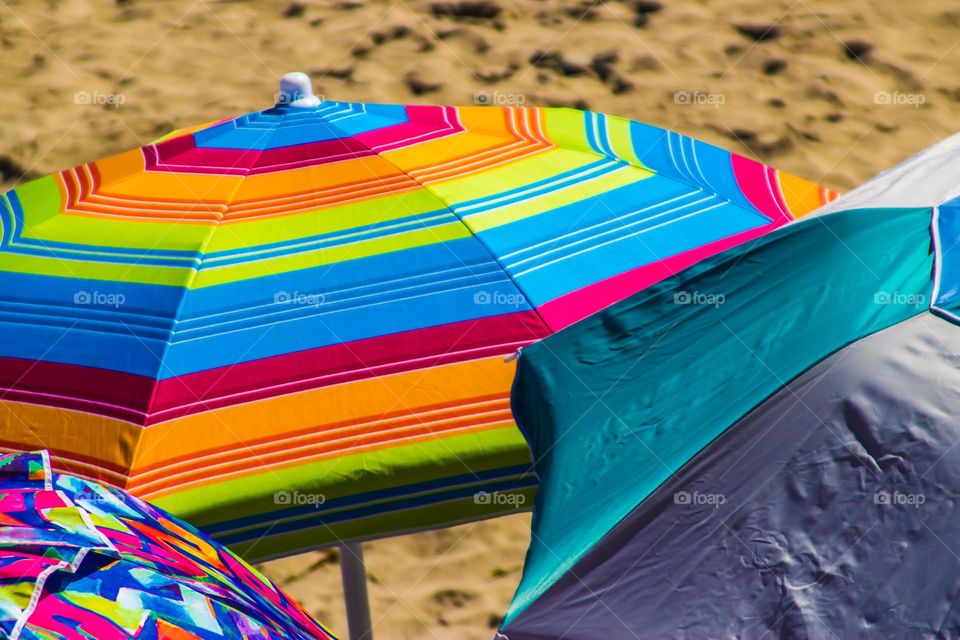 Very colorful beach umbrellas lounging on the beach with beautiful soft supple sand on a warm summer’s day 