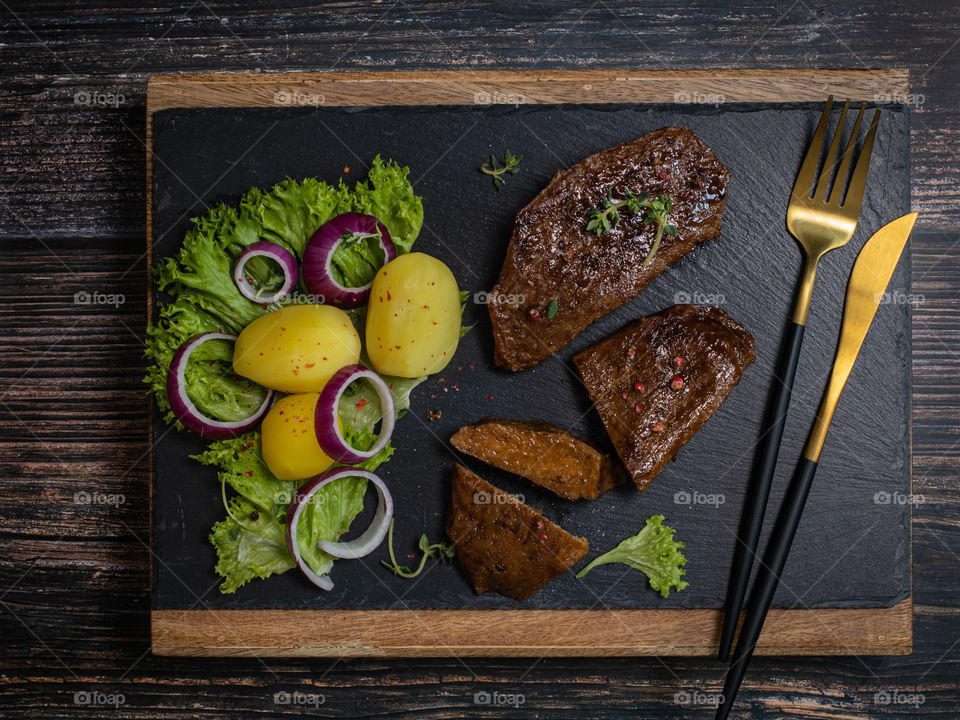 Vegan steak kn a black plate served with potatoes and fresh salad 