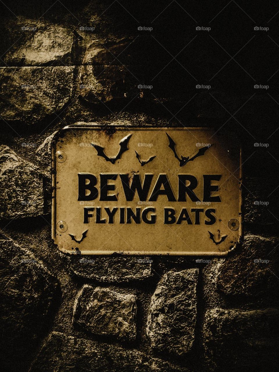 Spooky beware of flying bats sign on a faux rock wall.