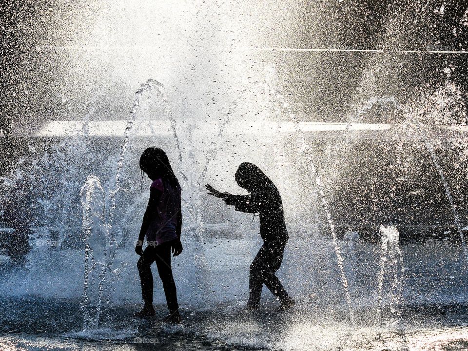 Two young girls enjoying the water fountain to beat the heatwave in the city