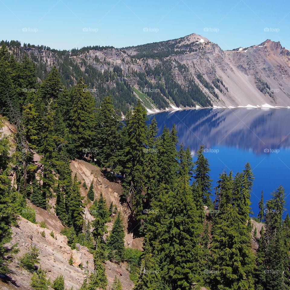 The rugged rim reflect in the stunning rich blue waters of Crater Lake in Southern Oregon on beautiful sunny summer morning. 