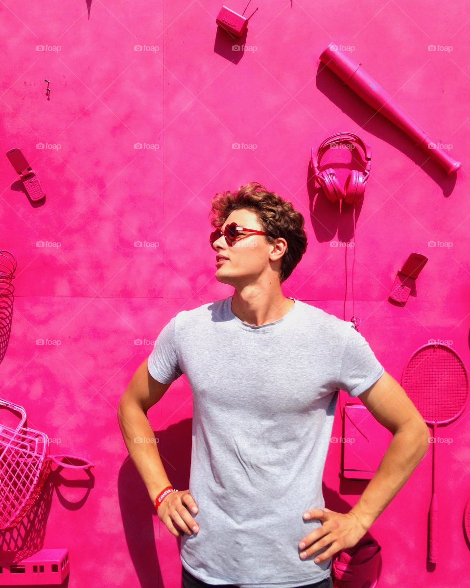 Young man standing against pink wall