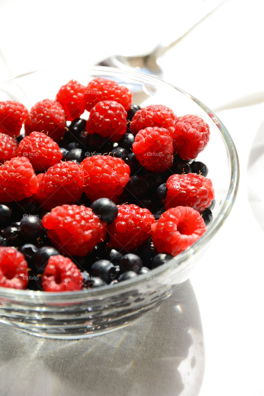 Bowl with fresh raspberries and blueberries  on sunny morning