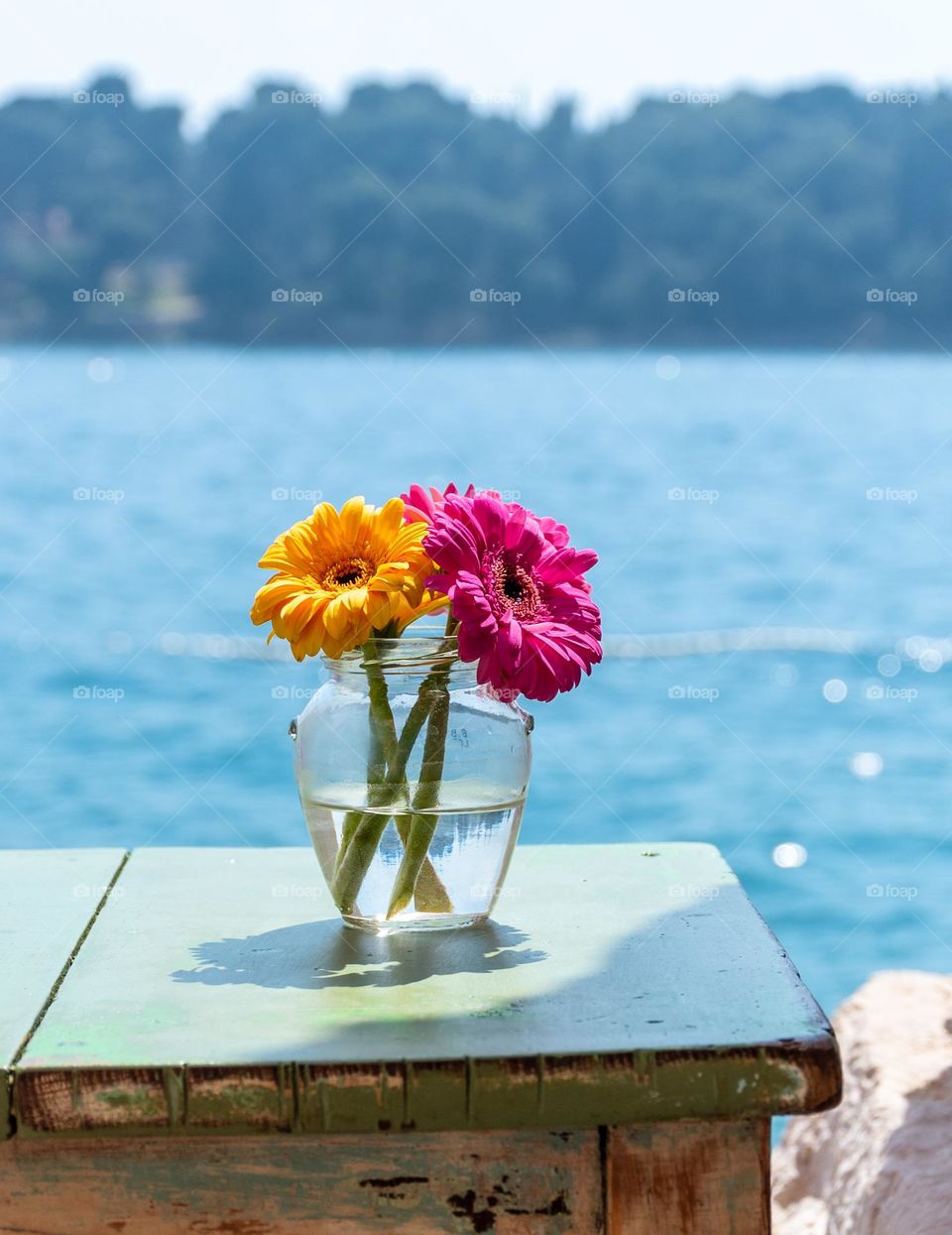 Colorful flowers in vase on table by the sea on a sunny day