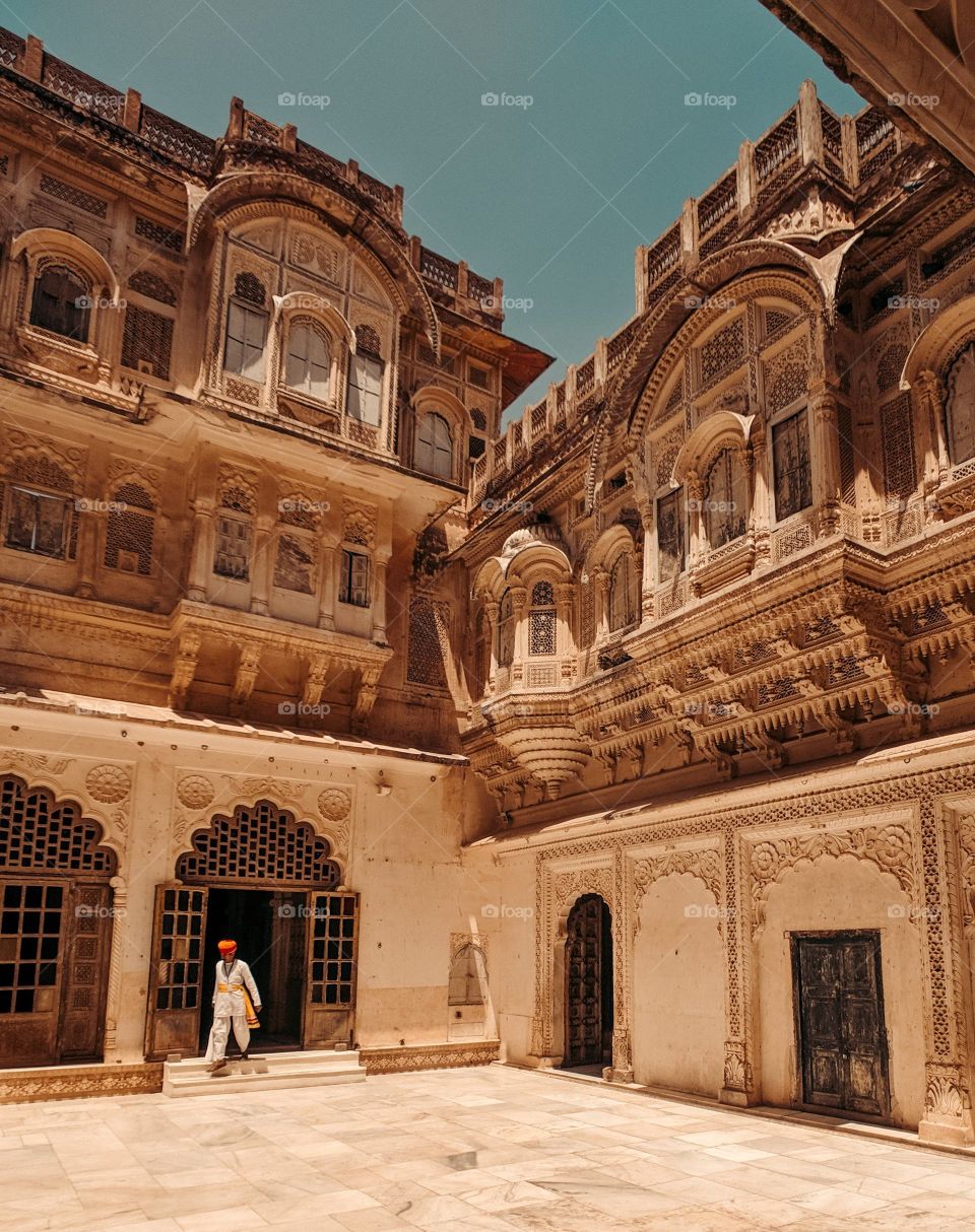 A person is seen walking out of a doorway to an intricate middle Eastern building that towers over the frame.