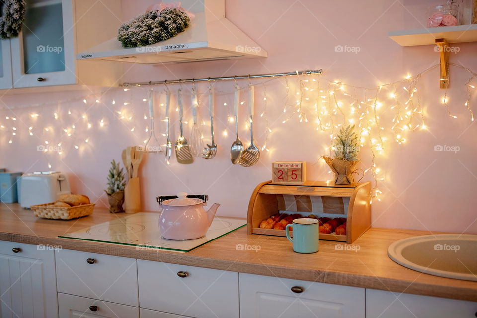 Festive winter cozy kitchen interior with garlands, decorations and gifts.  Christmas dinner at the decorated table.