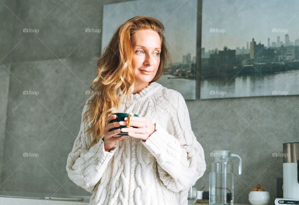 Young woman with long hair with cup of coffee tea in hands in kitchen at home 