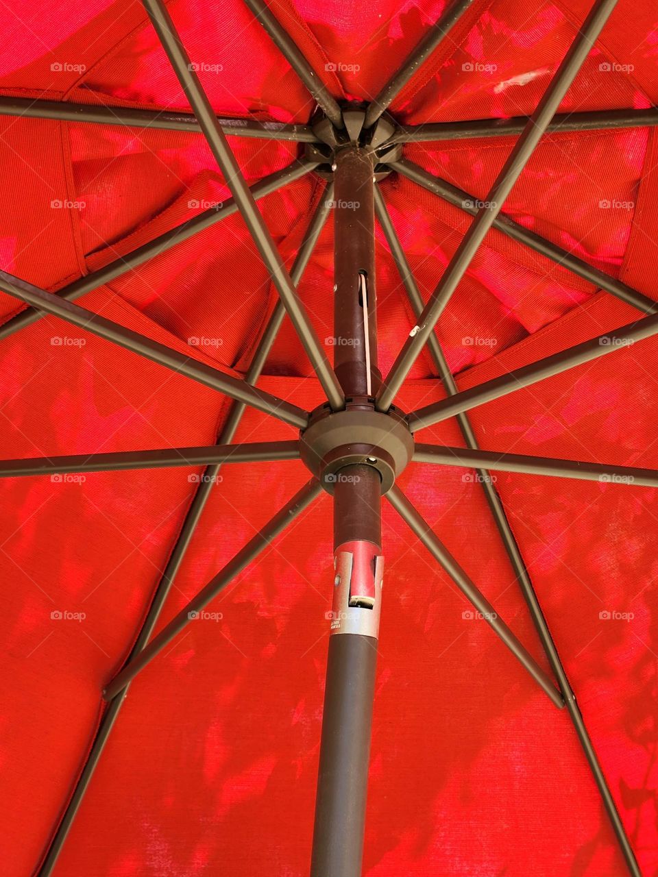 A view underneath a bright red umbrella providing shade from the Summer sun and shadow patterns of trees