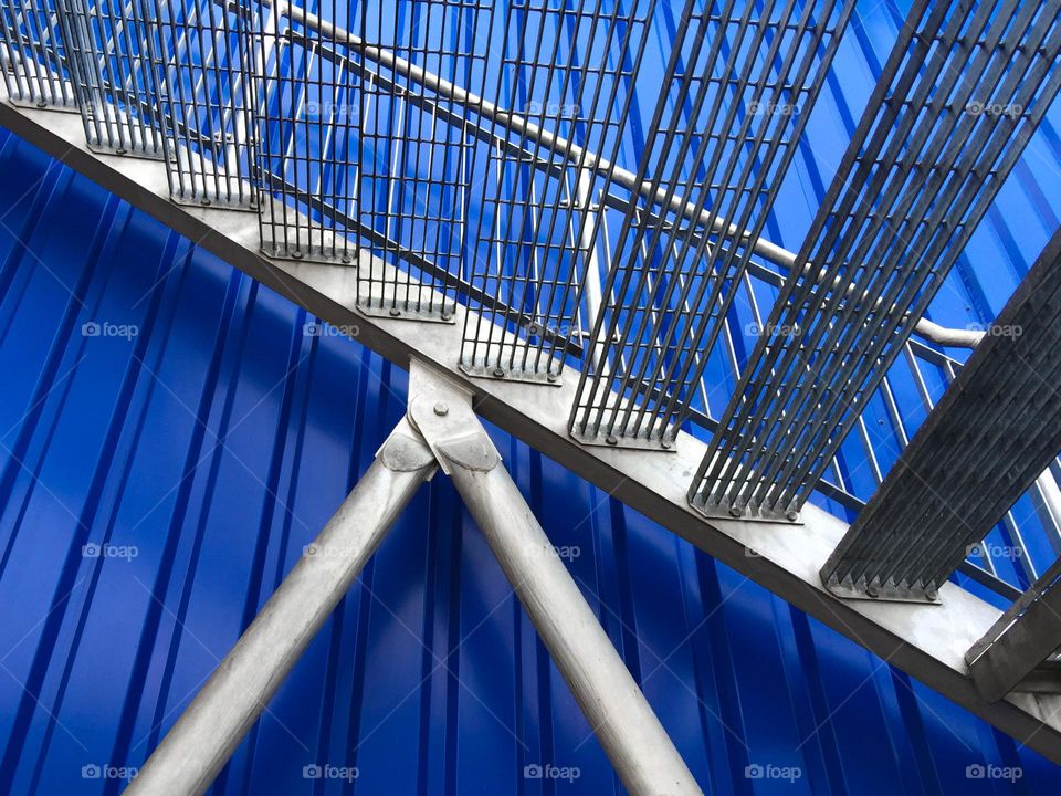 Close-up detail of galvanised steel staircase against blue metal cladding