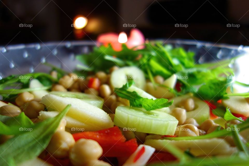 Fresh green salad. Fresh green salad including cucumber, apple, chickpea, paprika and arugula served on a glass bowl with candle.