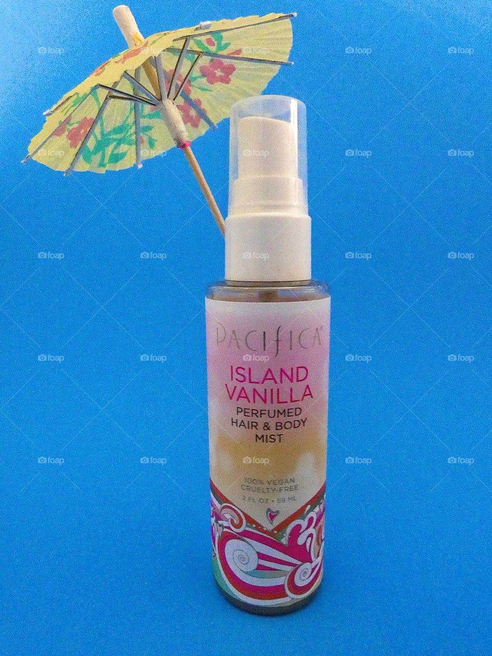 A bottle of Pacifica island vanilla perfumed hair and body mist spray on a blue background