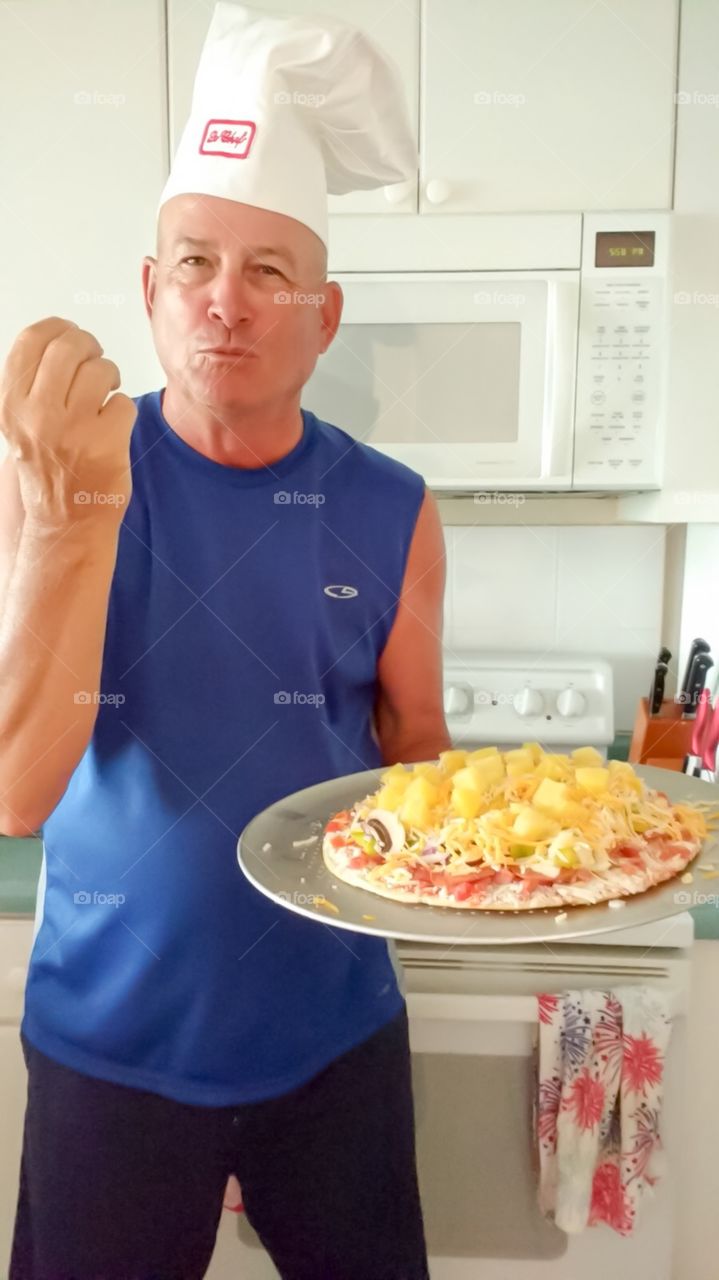 Home cook pizza chef, man in chef hat holding homemade pineapple pizza