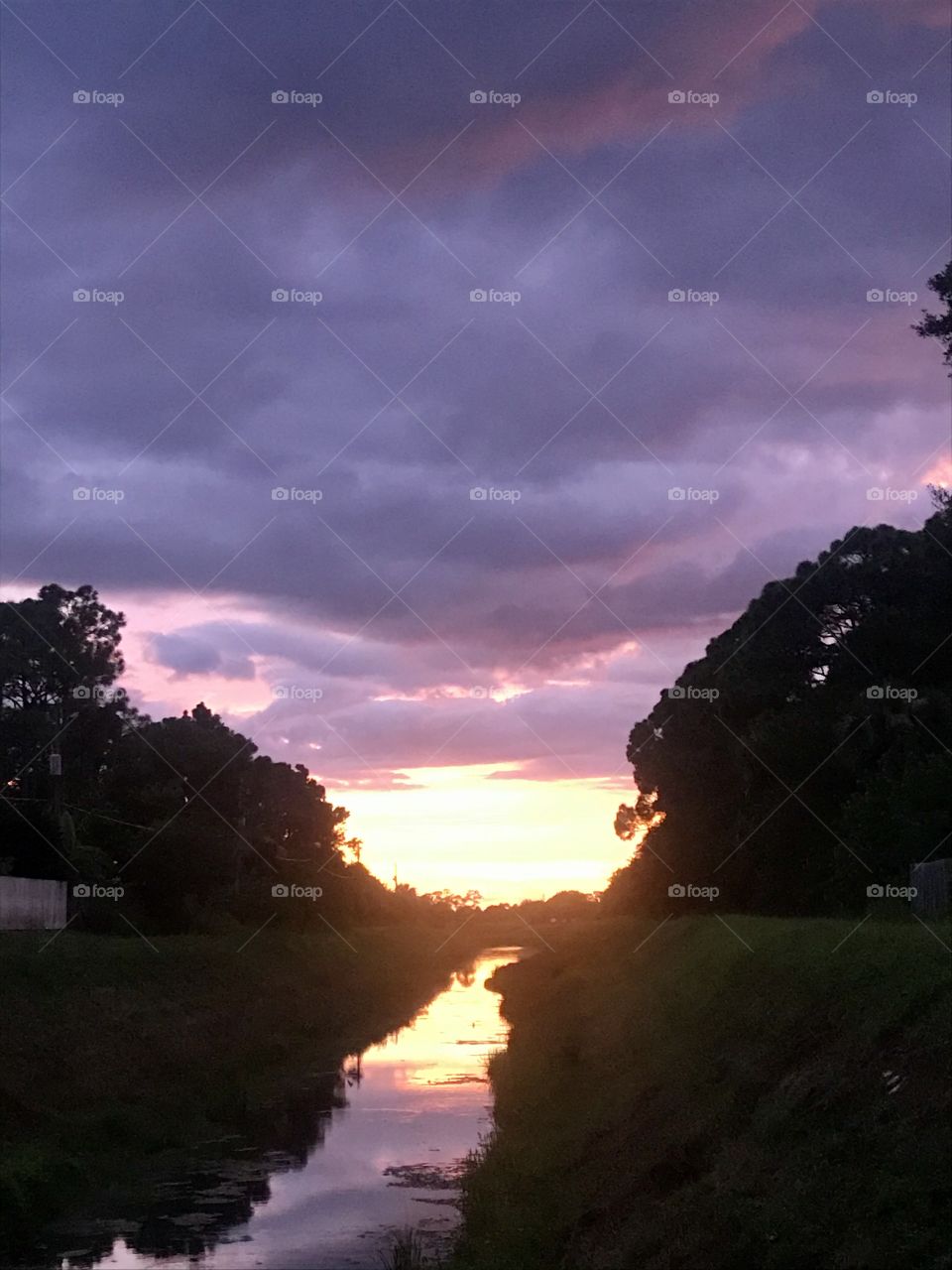 Sunset reflecting on water in a canal with purple clouds