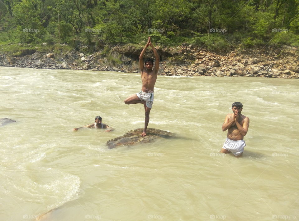 Yoga man standing one's leg on rock in the river