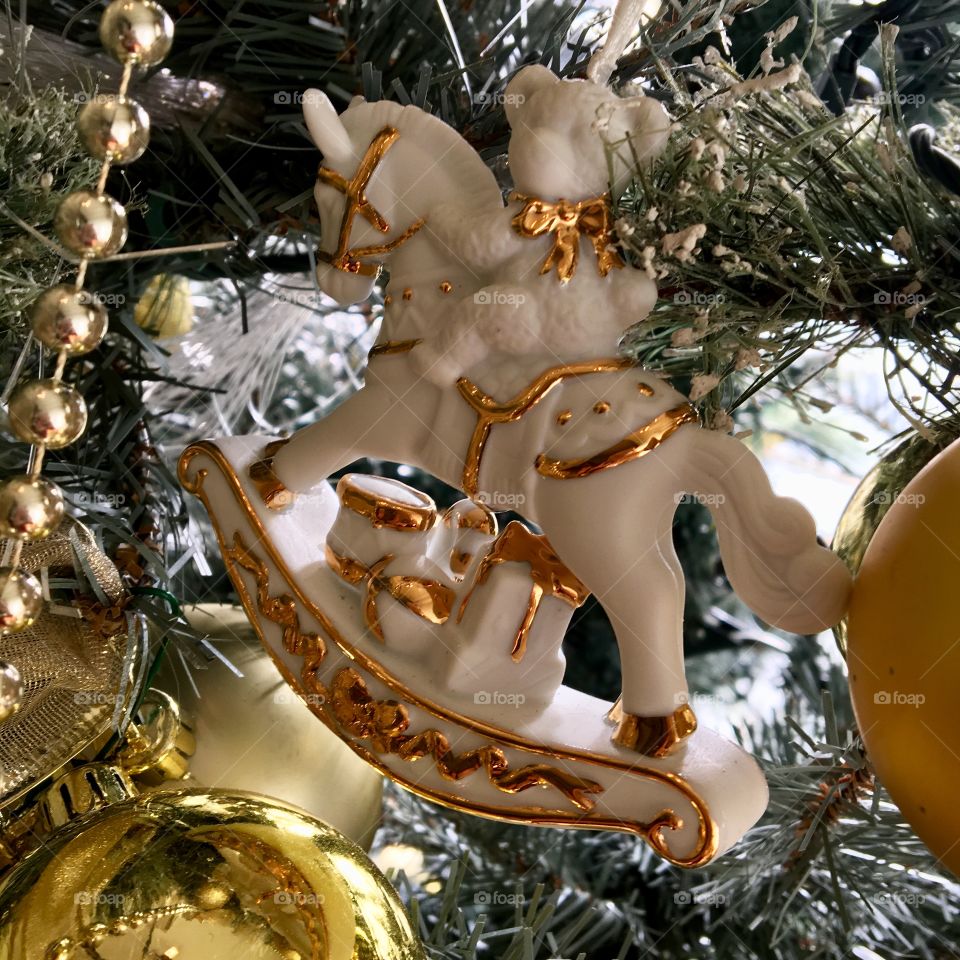 A teddy bear rides a rocking horse in this whimsical white-and-gold Christmas tree ornament.