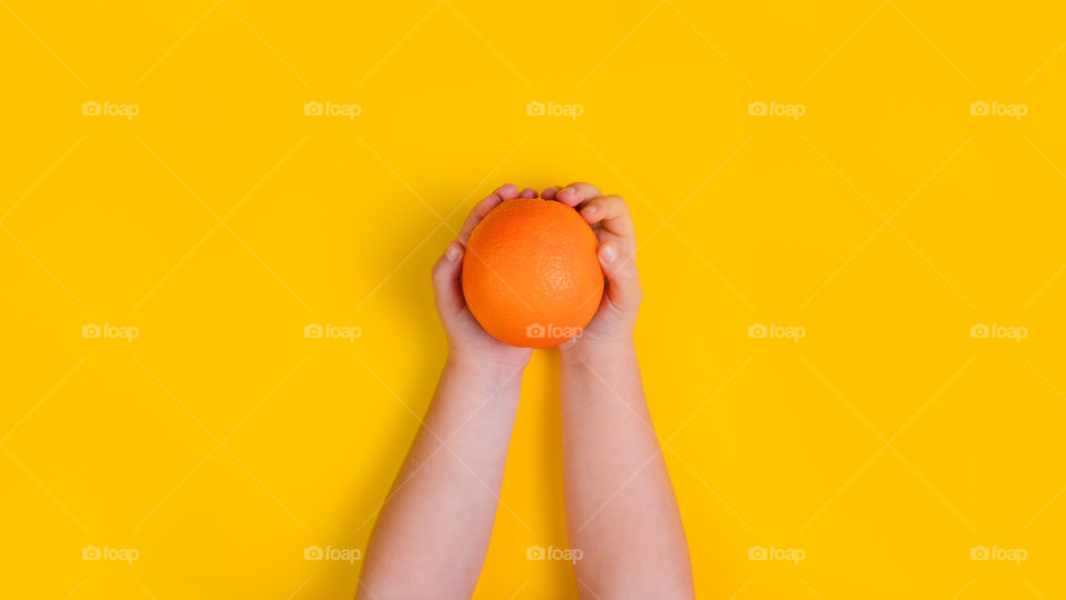 Hands of little girl with orange fruit on orange background. Top view. Copy Space