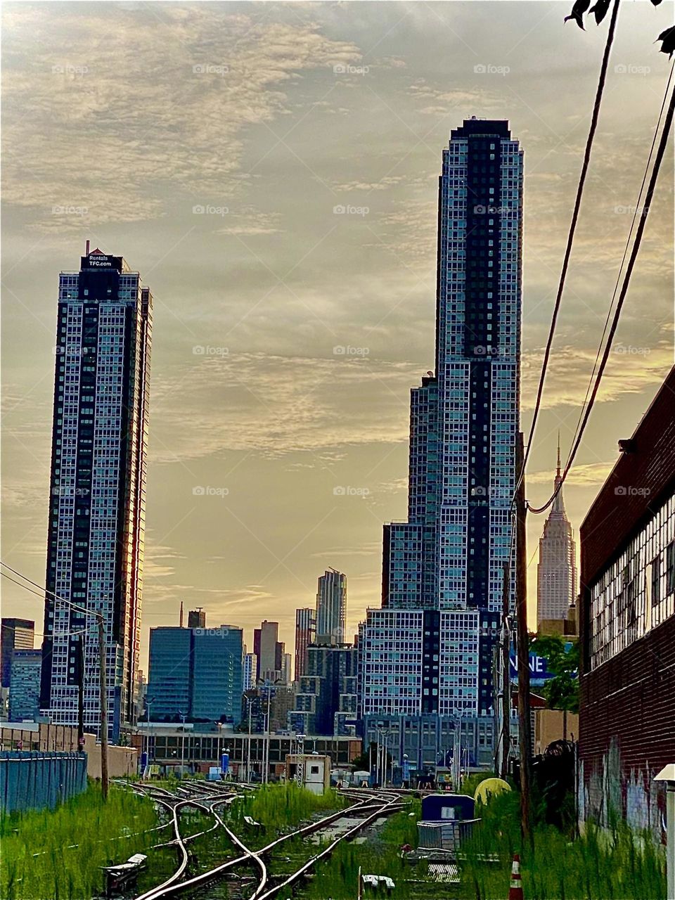 The train tracks by the „Pulaski Bridge“ just off „Borden Ave“ photographed against a backdrop of the setting sun during the golden hour are in the shade contrasting against the fiery drama in the sky. 2022. Hypnotic Productions