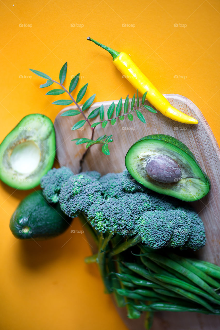 Broccoli, avocado and chili pepper on yellow background, healthy food