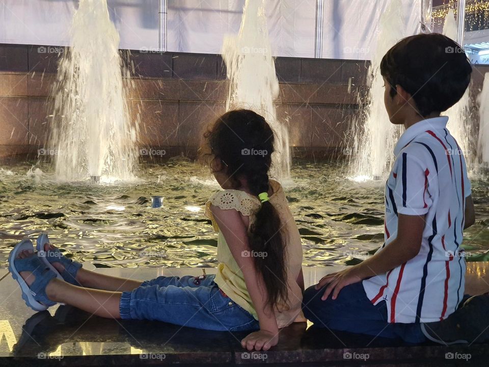 two kids watching at water fountain at night