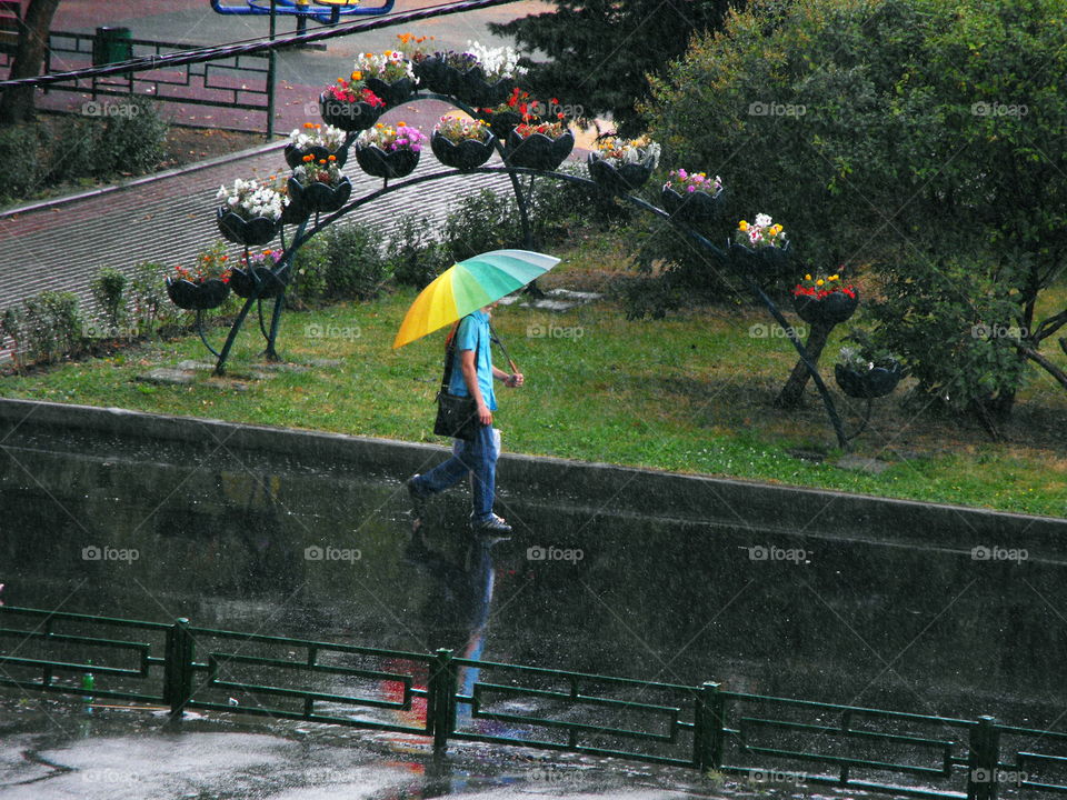 Somebody walking in a rain with a rainbow umbrella