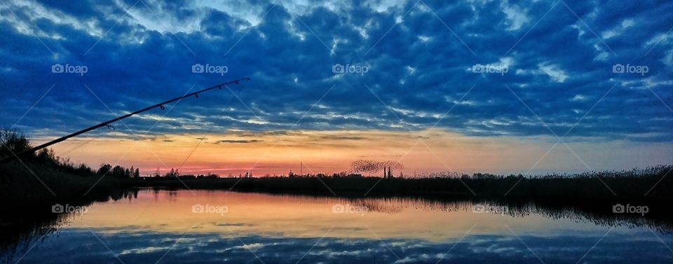 Nice cloudy evening sunset, with some birds in the background and fisherman near by.